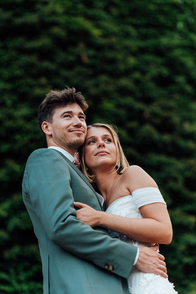 Photographe de mariage maine et loire 49 avrillé un air de famille couple de mariés enlacés avec le regard loin et en font de la verdure