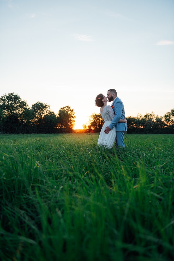 Photographe angers mariage poses couple Couple dans un champs d'herbes longue s'embrasse devant un couché de soleil
