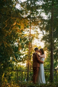 couple qui s'enlace dans un bois avec un coucher de soleil derriere